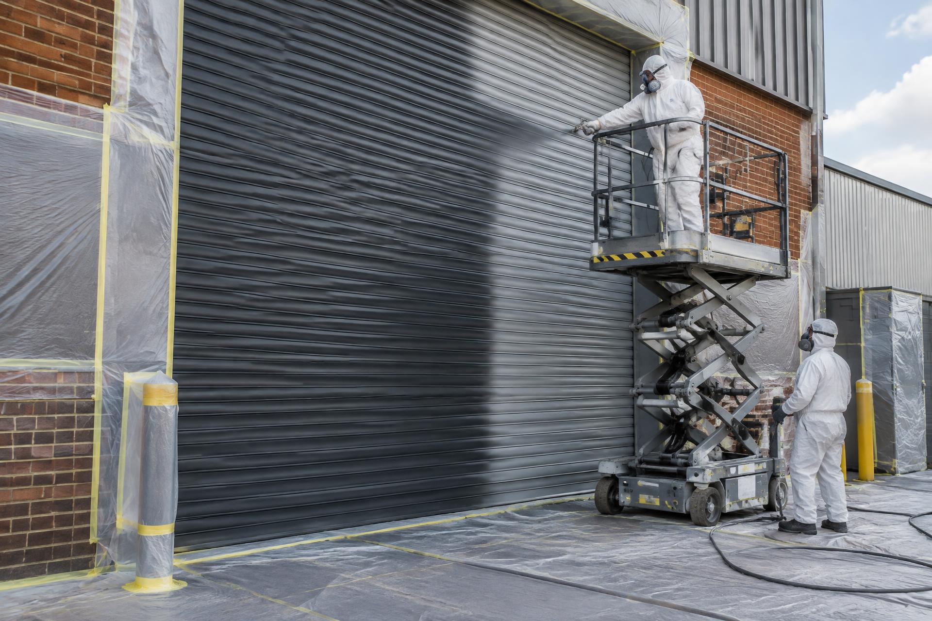 Illustrative view of technicians spray coating a masked industrial roller shutter